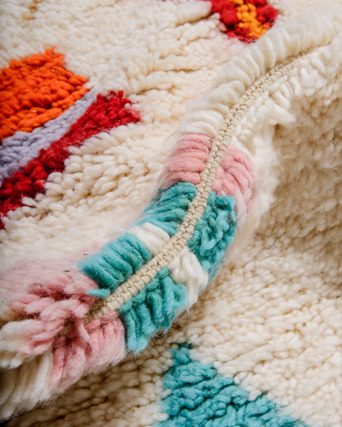 Detail of rug made of fluffy wool in cream, pink, turquoise, red and orange.